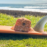 SurfShell portective surf hat in costal boho orange and floral shown on a surf board on grass