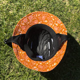 SurfShell Coastal boho protective surf hat with orange floral pattern, black chin strap and built-in impact protection insert, shown on grass.