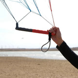 A person holding a Parawing bar with a bungee grey hanress line attached wiht a beach and the ocean in the background