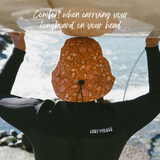 SurfShell portective surf hat in coastla boho burnt orange floral with surfboard on head to show comfort when wearing for carrying a surf board