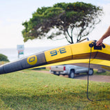 A yellow and black inflatable wing with grey graphics  and yellow allula material is being held on a grassy outdoor area near the ocean, with a persons holding it in place. with ozone 